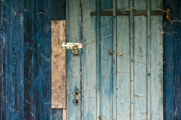 blaue tükise alte Holz Bretterwand enes Schuppens mit verschlossener und verriegelter Tür  mit rustikaler Holzmaserung, Vorhängeschloss und vielen kleinen Spinnennetzen