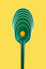 Green plastic picnic spoon on a yellow background
