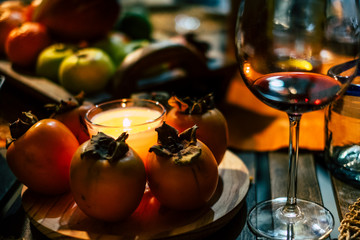 Winter style close up table with persimon fruits and red cup of wine - dark shadows and candle light for amazing evening atmosphere - christmas and new year eve concept -