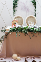 Wedding presidium in restaurant, free space. Wedding banquet table for newlyweds with flowers, greenery, pink cloth and bulbs. Lush floral arrangement on wedding table. Luxury wedding decorations