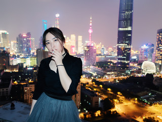 Portrait of beautiful Chinese girl in black dress smoking a cigarette outdoor with Shanghai skyline background at night.