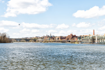 Cityscape, skyline view of Potomac river, Georgetown waterfront park in Washington, DC, District of Columbia, water waves, helicopter flying on sunny spring day, Whitehurst freeway, blue sky ,clouds