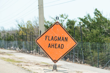 Flagman ahead traffic road sign in red, orange color, signal for drivers on overseas highway road, US1 about utility, construction, repair work, workers