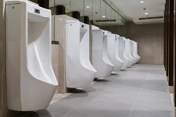 The toilet of man with Row of modern white ceramic urinals in public toilet or restaurant or hotel...