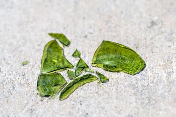 Closeup of many shattered, broken pieces, fragments, parts of green glass bottle on ground, sidewalk pavement, asphalt