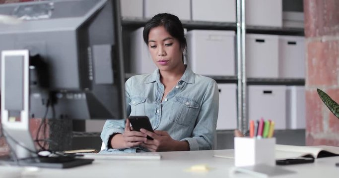 Young adult female working in an office looking at a smartphone