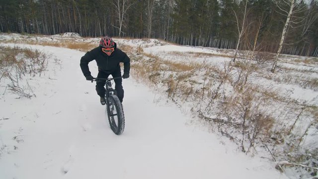 Professional extreme sportsman biker riding fat bike in outdoors. Cyclist ride in winter snow forest. Man does trial trick wheelie on mountain bicycle with big tire in helmet and glasses.