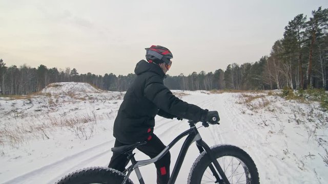 Professional extreme sportsman biker walk with fat bike in outdoors. Cyclist walking in the winter snow forest. Man go on mountain bicycle with big tire in helmet and glasses. Slow motion in 180fps.