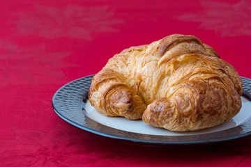 Fresh croissant on a white and bronze stoneware plate on red tablecloth