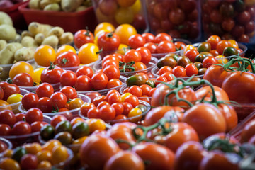 Cherry tomatoes of different sizes dans colors, red yellow and green, for sale on a canadian market of montreal, displayed in plastic baskets and punnets.