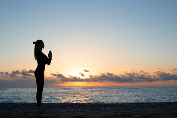 silhouette of woman doing greeting to the sun on the beach at sunrise, morning yoga