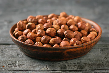 A clay bowl full of walnut kernels on a dark rustic table. Vegetarian cuisine.