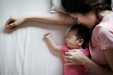 Close up portrait from top view of beautiful young Asian mother kissing her newborn baby sleeping in bed in the morning. Healthcare and medical love lifestyle of mother and baby concept.