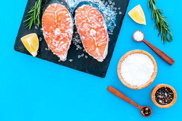 Fresh salmon steak with spices, rosemary, lemon for cooking healthy food on blue background top view mock-up