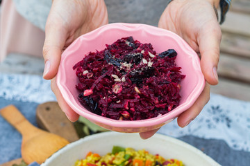 Grated beetroot salad with dried plum, seeds and garlic. Vegan vegetarian healthy food. Woman hands holds fresh beetroot salad.