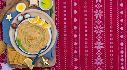 Chickpea hummus dip paste with corn crispy bread, olive oil. Space for text. Christmas food lunch or dinner on red background tablecloth with decoration on wooden board. Vegan vegetarian healthy food
