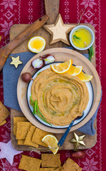 Chickpea hummus dip paste with corn crispy bread, olive oil as Christmas food lunch or dinner on red background tablecloth with decoration on wooden board. Vegan vegetarian healthy food