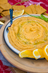Chickpea hummus dip paste with corn crispy bread, olive oil as Christmas food lunch or dinner on red background tablecloth with decoration on wooden board. Vegan vegetarian healthy food