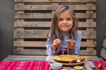 Chickpea hummus dip paste with corn crispy bread, olive oil. Little smiling girl eats Christmas food lunch or dinner on red background tablecloth with decoration on wooden board. Vegan healthy food