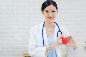 Young woman doctor holding a red heart, standing on brick wall background