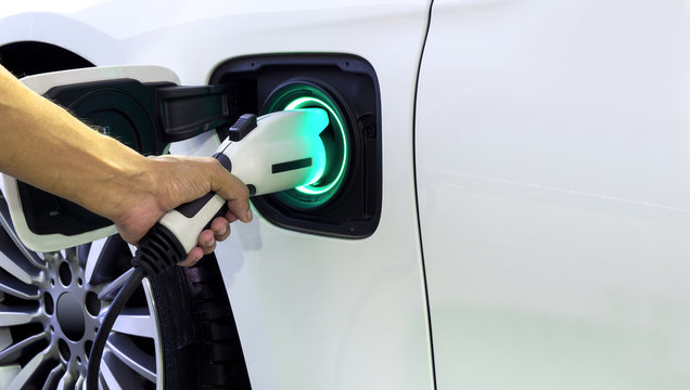 Hand of man holding plug for charge electric power into Battery of Electric car  on charge station electric mobility environment friendly with copy space.