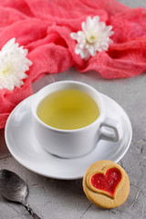 A cup of green tea and cookies with hearts on a gray background. Beautiful still life with a cup of tea, the mood of Valentine's Day.