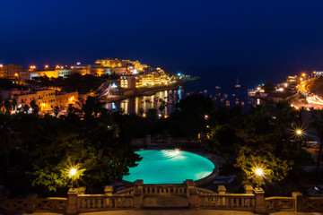 View of St. George's Bay seafront lights by night, with a blue luxury swimming pool and boats and...