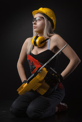 blonde girl in overalls posing with an electric saw