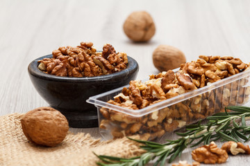 Walnuts in stone bowl and plastic container on a wooden background.