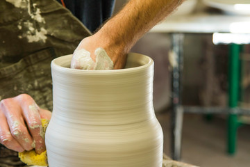 Fototapeta na wymiar Artist potter in the workshop creating a ceramic vase. Hands closeup. Twisted potter's wheel. Small artistic craftsmen business concept. 