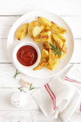 Potato baked and tomato ketchup on white plate, wooden background, top view