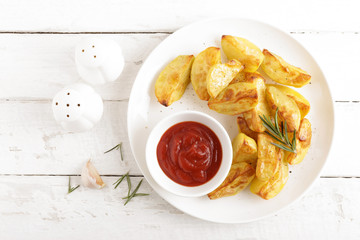 Potato baked and tomato ketchup on white plate, wooden background, top view