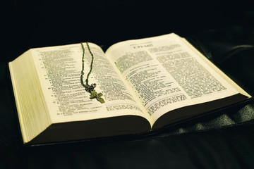 Obraz premium black background, on the open bible lies a metal cross