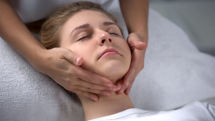 Fototapeta na wymiar Experienced cosmetologist making girl relaxing face massage, treatments