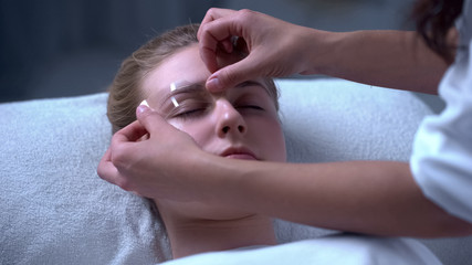 Make-up artist applying stencil on clients eyebrows, services of cosmetologist
