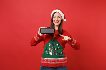 Smiling young Santa girl pointing index finger on portable wireless bluetooth music speaker...