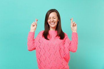 Cute young woman in knitted pink sweater keeping fingers crossed eyes closed make wish isolated on blue wall background studio portrait. People sincere emotions, lifestyle concept. Mock up copy space.