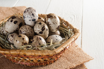 Obraz premium Several mottled quail eggs on straw in basket on wooden background