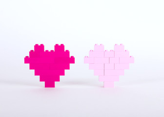 The bricks of the plastic constructor in the form of hearts are red, magenta, pink. White background.