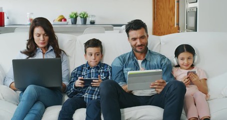 Portrait of happy family having fun using different modern media devices on sofa in living room in slow motion. 