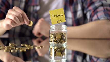 Travel word written above glass jar with money, savings for summer vacation