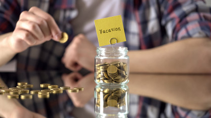 Fototapeta premium Vacation word written above glass jar with money, savings for summer holidays
