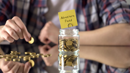 Adventure fund phrase above glass jar with money, savings for hobby, interests