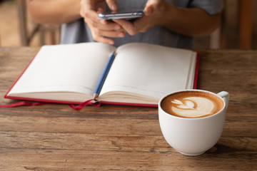 Woman checking her work on smart-phone blurred on background with warming drink, Late coffee in a cup in front-of on wooden table on-line working concept design