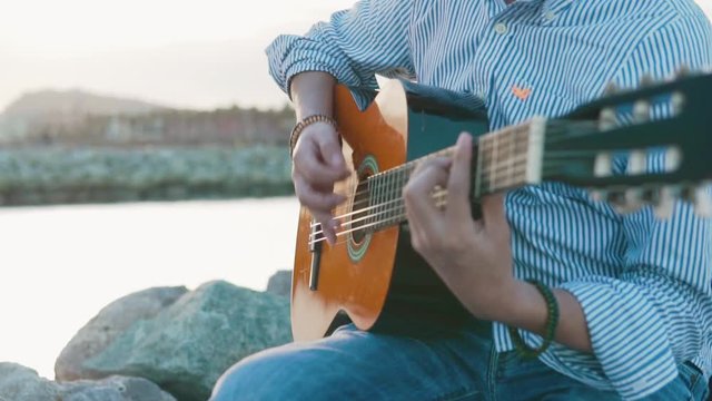 slowmotion shot of of musician man playing acoustic guitar and sing near the beach. Sea on background