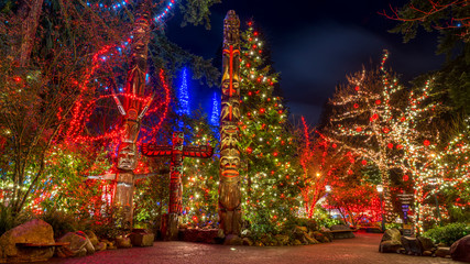 Totem poles seen at night with Christmas lights in the background. Capilano Bridge, Vancouver. Beautiful British Columbia, Canada.