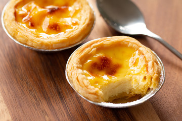 Egg tarts in aluminum foil cup on wood table,  traditional Portuguese dessert served in coffee shop