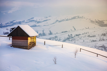 outskirts of the village on the hill. woodshed behind the wooden fence on a snowy slope. peaks of the distant mountain ridge in clouds. wonderful winter tale in gorgeous light