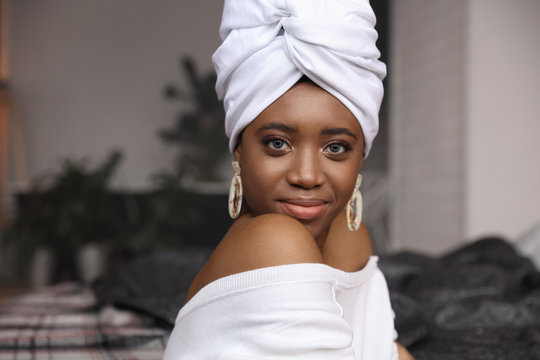 Beauty portrait of young woman dressed in white head tie, white sweater and big earrings, african bracelets. Interior studio