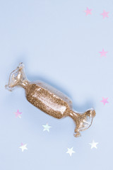 Toy in the shape of holidays candy with the gold glitter and glitter stars on a blue background.